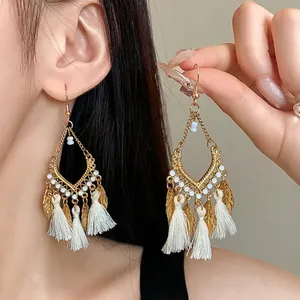 Orecchini pendenti boho con foglie dorate e nappe bianche indossati da una modella