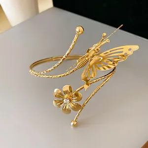 Close-up of a gold cuff bracelet featuring a hollow butterfly and a crystal flower