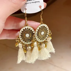 Dettaglio di orecchini bohémien rotondi con motivo a sole in smalto bianco e nappe