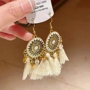 Dettaglio di orecchini bohémien dorati con mandala bianco e nappe di filo bianco