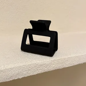 Primo piano di una piccola molletta per capelli quadrata nero opaco su sfondo materico