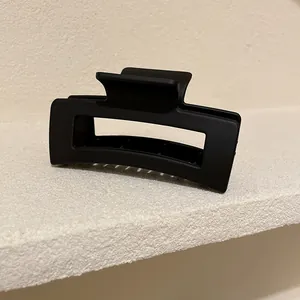 Vista dettagliata di una pinza per capelli nera opaca minimalista su bordo in pietra