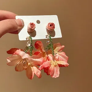 Hand holding sweet floral mesh tassel earrings with pink roses and green beads