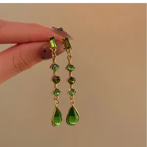 Élégantes boucles d'oreilles pendantes en or avec zircons verts et long pompon.