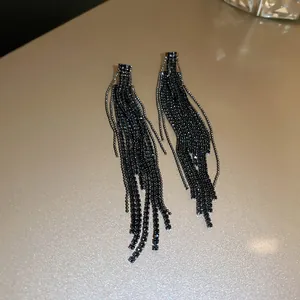 Detailed macro view of elegant black rhinestone tassel drop earrings on a golden surface.