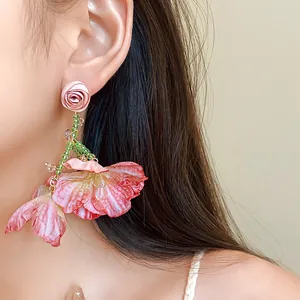 Close-up of elegant pink mesh flower earrings with green bead tassels on model.