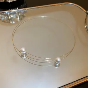 Close-up of minimalist double-wire choker necklace with two elegant pearls on a mirror