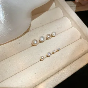 Detail view of multiple sizes of round white pearl stud earrings on a beige tray