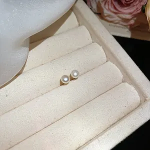Exquisite macro detail of elegant white pearl stud earrings on a beige jewelry display tray