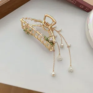Detailed view of an elegant gold hair claw clip featuring lily of the valley and pearl tassels