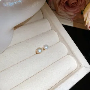 Elegant round pearl stud earrings showcased in a beige velvet jewelry box tray.