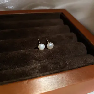 Close-up detail of round white pearl stud earrings on silver pins in a brown velvet jewelry box