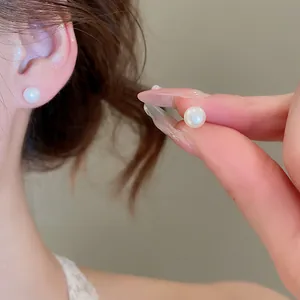 Elegant round pearl stud earrings shown as worn on ear and held between fingers