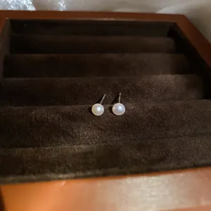 Macro detail of round white pearl stud earrings with silver needles in a jewelry box.