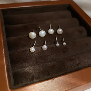 Detail of four pairs of round pearl stud earrings in different sizes on brown velvet