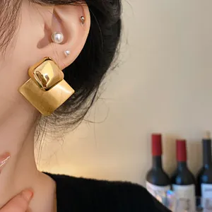 Close-up of gold-plated brushed diamond earrings showing metallic texture on model.
