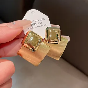 Macro detail of brushed gold plated rhombus stud earrings with glossy square accents