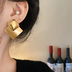 Close-up view showing the textured brushed finish of gold-plated geometric diamond stud earrings.