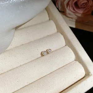 Close-up detail of elegant round pearl stud earrings presented on a soft beige jewelry tray