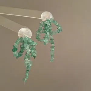 Macro view of bow earrings crafted with green natural stone chips and white shell studs
