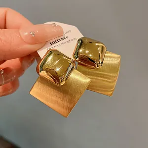 Close-up of gold plated square earrings featuring glossy and brushed textures.