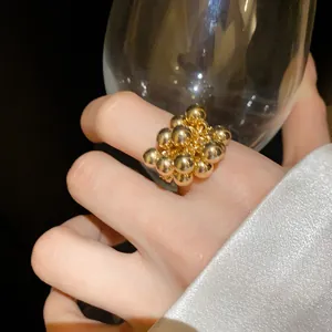 Primo piano dettagliato di un anello a grappolo d'oro su una mano che tiene un bicchiere.