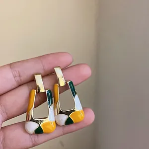 Macro view of geometric square earrings with colorful enamel sections in a hand