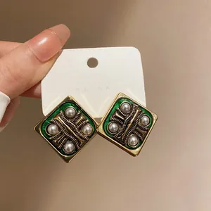 Close-up of vintage square geometric earrings with green enamel and faux pearl accents