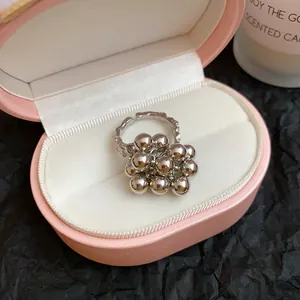 Primo piano di un anello aperto in argento con perline metalliche in una scatola rosa.