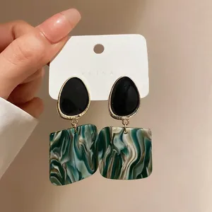 Close-up of green marble acrylic square earrings with black oval stud detail