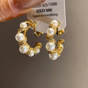 Vue macro de boucles d'oreilles clips dorées 18k en forme de C avec perles blanches et zircons