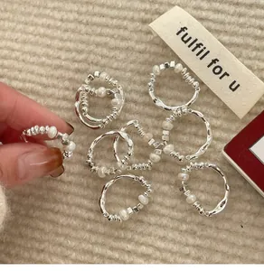 Close-up of irregular pearl and silver bead elastic rings on textured beige fabric