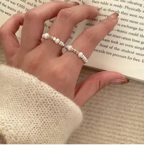 Detailed view of minimalist irregular pearl elastic rings on model's hand with book