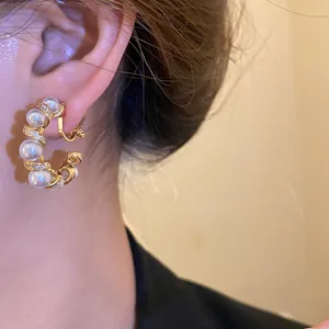 Gros plan d'un clip d'oreille en C doré 18k avec perles et zircons porté à l'oreille