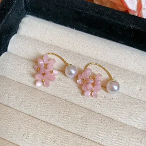 Close-up of elegant pink flower and pearl earrings displayed in a beige jewelry box