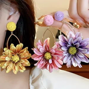 Macro detail view of colorful fabric and raffia flower earrings worn by a model