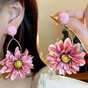 Close-up of bohemian pink fabric flower earrings with woven raffia studs on ear