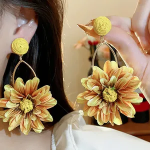 Detailed view of yellow raffia fabric flower earrings with elegant gold metal hoops.