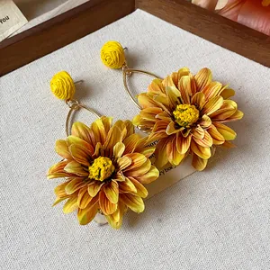 Close-up detail of yellow fabric and raffia flower earrings with elegant golden hooks