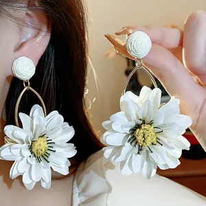 Detailed view of white fabric daisy earrings with raffia rose studs and golden hoops