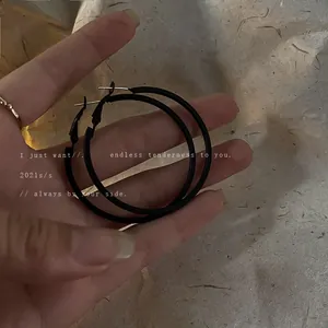 Minimalist large black metal hoop earrings held in hand with a textured paper background