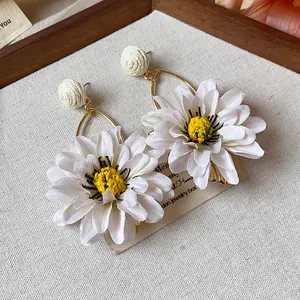 Detailed macro view of elegant white fabric flower earrings with woven raffia beads