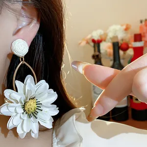 Close-up detail of elegant white fabric flower earring with raffia stud on a model's ear