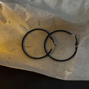 Close-up of minimalist black matte metal hoop earrings on textured paper.