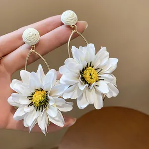 Close-up of white fabric flower earrings with yellow centers and raffia studs.
