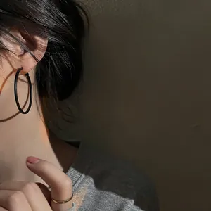 Detailed view of stylish black metal hoop earring worn by a model in soft lighting
