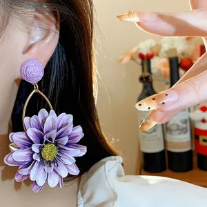 Detailed close-up showing a purple fabric flower earring with unique raffia texture worn on ear