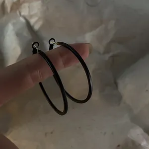 Close-up detail of oversized dark brown geometric metal hoop earrings on finger