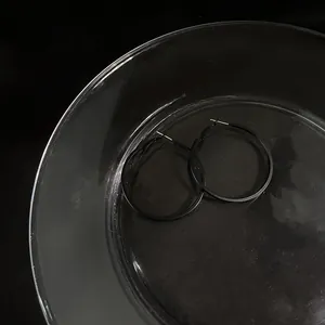 Close-up detail of minimalist black metal hoop earrings placed on a clear glass tray
