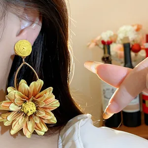 Close-up of vacation style yellow raffia fabric flower drop earrings worn on ear.